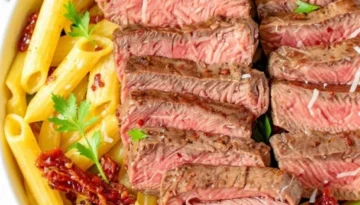 Delicious Steak Pasta Recipe: Quick & Easy Weeknight Meal Close-up of a bowl of steak pasta, featuring perfectly cooked penne pasta, sliced medium-rare steak, sun-dried tomatoes, fresh spinach, and grated Parmesan cheese, garnished with fresh parsley and red pepper flakes.