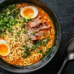 A bowl of spicy birria ramen with tender meat, ramen noodles, soft-boiled eggs, and fresh garnishes