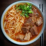 A steaming bowl of birria ramen with tender meat, ramen noodles, and fresh green onions.