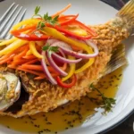A vibrant plate of Jamaican Escovitch fish with colorful pickled vegetables and a side of crispy fried fish.