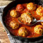 Homemade chicken meatballs simmering in a rich marinara sauce in a cast iron skillet, garnished with fresh herbs.