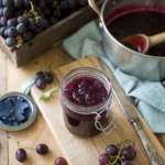 Jar of homemade grape jelly on a wooden tray with bread and butter.