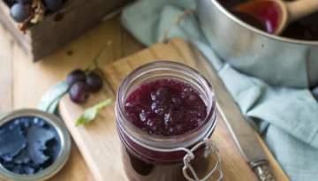 Hero Image Jar of homemade grape jelly on a wooden tray with bread and butter.