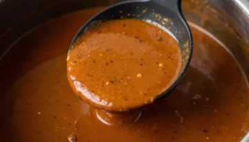 Perfect Homemade Gravy Recipe: Smooth, Rich & Flavorful Close-up of rich, brown homemade gravy being ladled from a gleaming stainless steel saucepan into a serving dish, showing its smooth texture and steam.