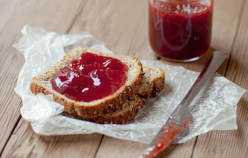 Easy Homemade Grape Jelly Recipe Classic Sweet Preserve Vibrant homemade purple grape jelly in clear glass jars on a rustic wooden surface, with a spoon showing its shimmering texture, ready for canning.